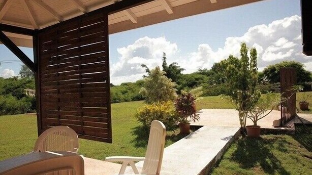 A covered outdoor seating area with a view of a landscaped garden and a clear sky.