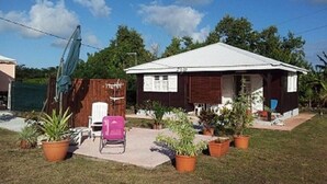 A small house with a white roof and a covered porch. There are several potted plants in front of the house.