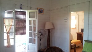 A room with a wicker chair, a standing fan, a lamp, and a door leading to an outdoor area.