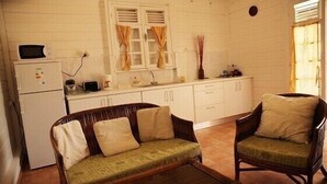 A compact kitchen with a refrigerator, microwave, and toaster. There are two wicker chairs with cushions and a small dining table.
