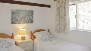 A bedroom with two single beds, a nightstand with a lamp, a painting on the wall, and a window with curtains. - An apartment situated in mature woodlands just 3 miles from Ambleside. (Skelwith Bridge, Ambleside)