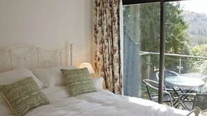 A bedroom with a large bed, a nightstand, and a view of a balcony with outdoor furniture. - An apartment situated in mature woodlands just 3 miles from Ambleside. (Skelwith Bridge, Ambleside)