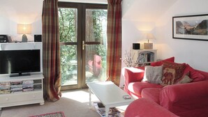 A living room with a television, a sofa, a coffee table, and a bookshelf. - An apartment situated in mature woodlands just 3 miles from Ambleside. (Skelwith Bridge, Ambleside)