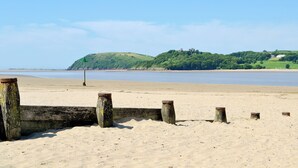 A sandy beach with wooden posts and a green sign, leading to a hill with a castle-like structure in the background. - 1 bedroom accommodation in Gowerton, Gower (Gowerton, Gower)
