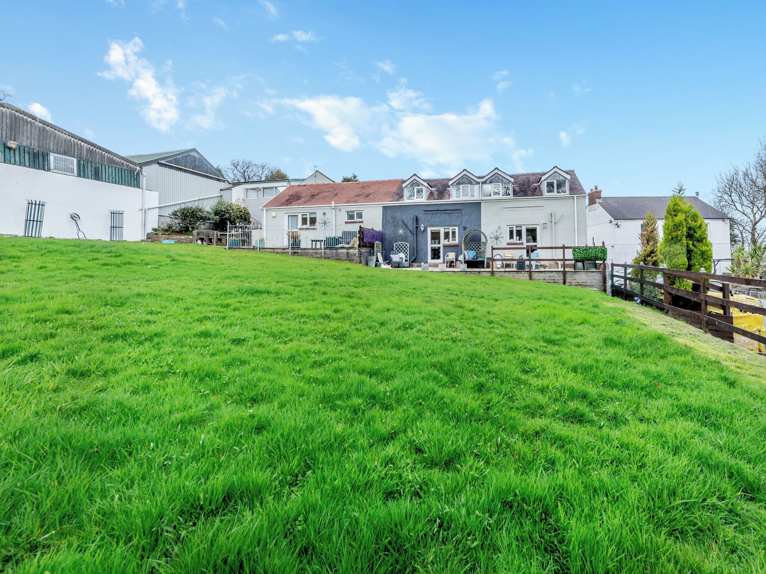 A residential building with a large grassy yard, a fenced patio area, and a white exterior wall.