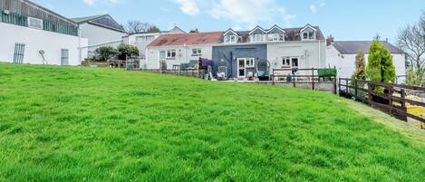 A residential building with a large grassy yard, a fenced patio area, and a white exterior wall.