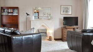 Ein Wohnzimmer mit Ledersofas, einem Kamin, einem Fernseher und einem Bücherregal.