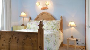 Ein Schlafzimmer mit einem hölzernen Bett, floraler Bettwäsche, zwei Nachttischlampen und einer Wandleuchte.