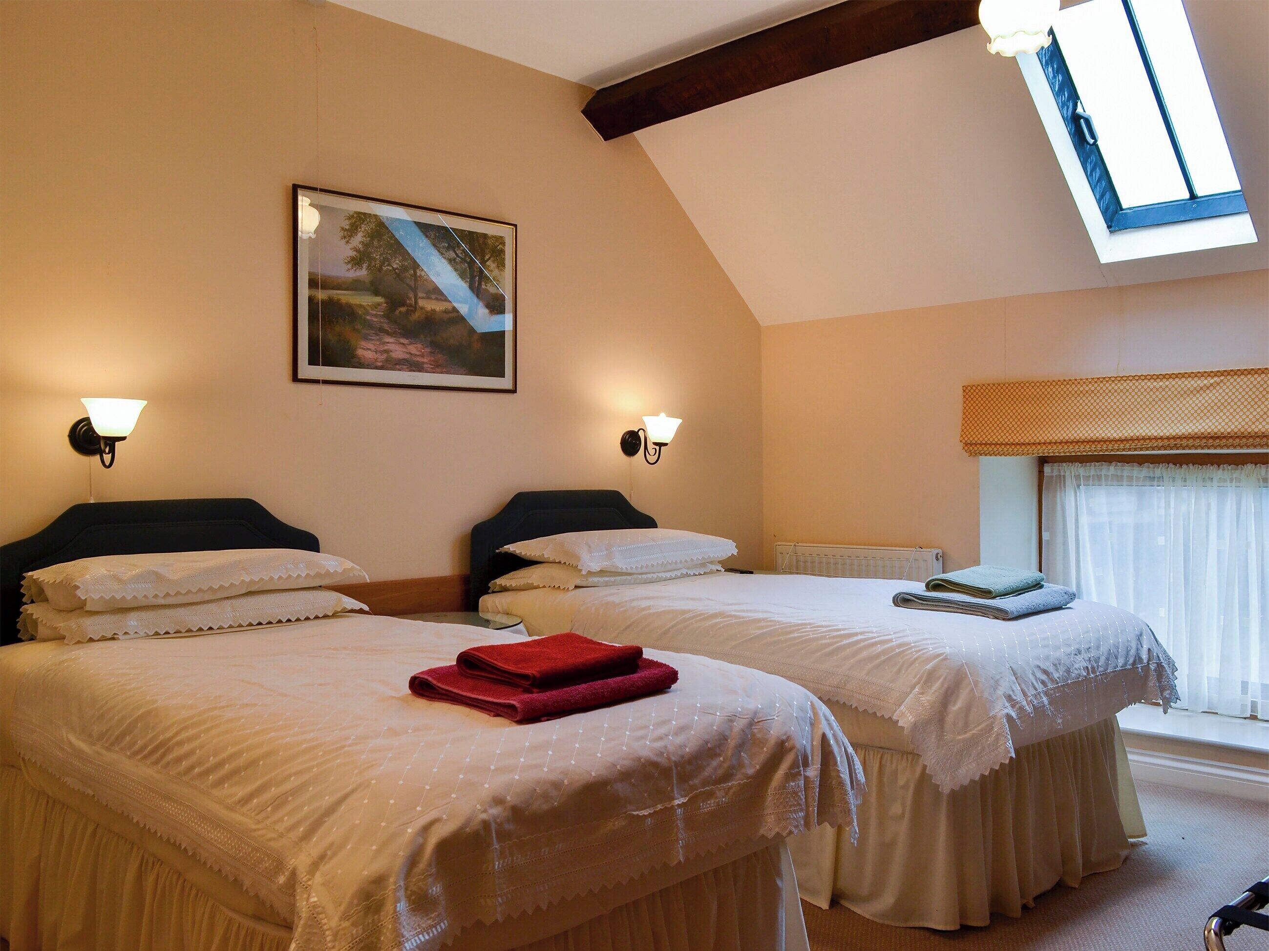 A hotel room with two beds, a skylight, a painting, and a radiator.