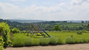 A grassy field with a wooden swing set and picnic table, surrounded by trees and hills in the background. - 3 bedroom accommodation in Broome Chatwall, near Church Stretton (Broome Chatwall, near Church Stretton)