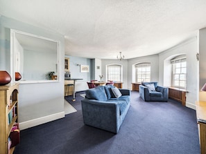 A spacious living room with a large mirror, two sofas, a dining area, and a kitchen in the background.