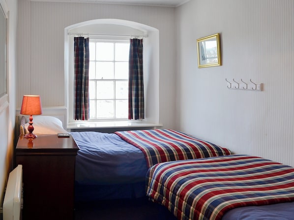 A room with a bed, a lamp, a window with curtains, a picture frame, and a coat rack.