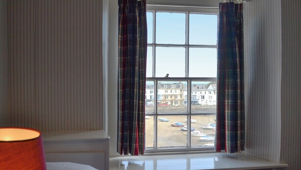 A room with a bed, a window with curtains, and a view of a parking area and buildings.