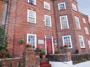 A red brick building with multiple windows, a red door, and flower pots on the steps.