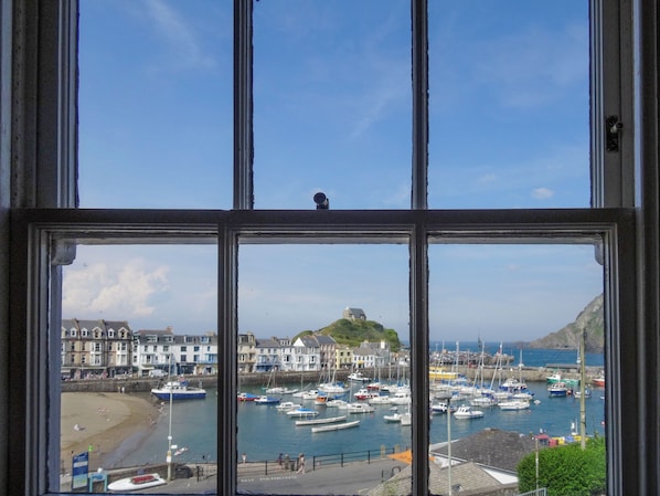A coastal town with a harbor, buildings, and a hill with a structure on top.