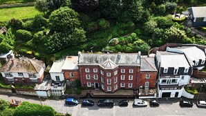 An aerial view of a town with a prominent red brick building, a parking lot, and surrounding greenery.