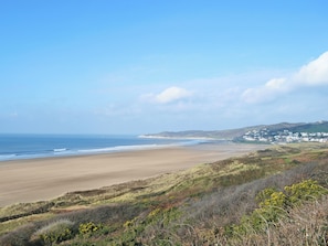 A coastal landscape with a sandy beach, rolling hills, and a small settlement in the distance.