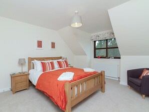 A bedroom with a wooden bed, a nightstand, a bedside table, a window with a view, and a dark-colored armchair. - 4 bedroom accommodation in Aviemore (Aviemore)