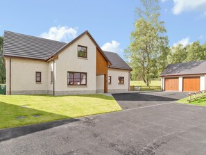 A two-story building with a sloped roof, a garage, and a well-maintained lawn. - 4 bedroom accommodation in Aviemore (Aviemore)