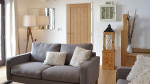 Un salon avec un canapé gris, une petite table, une lampe, un meuble en bois et un miroir au mur.