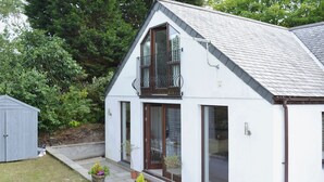 Un bâtiment blanc avec un toit en pente, un balcon et une porte dotée de panneaux de verre.