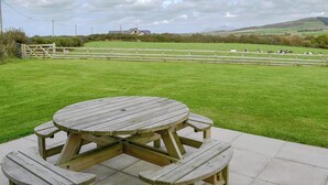 Una mesa de picnic en un campo cubierto de hierba, con vistas a una casa y ovejas a lo lejos.
