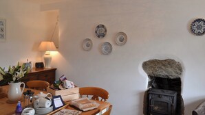Un comedor acogedor con una mesa de madera dispuesta para una comida, una estufa antigua y platos decorativos en la pared.