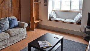 Una sala de estar acogedora con una escalera de madera, un banco empotrado con almohadones, una mesa de centro negra y un ventanal con vistas.