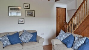 Una sala de estar con dos sofás beige, cada uno con cojines de estampado azul, y una escalera de madera al fondo.