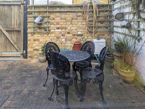 A patio with a round table and four ornate chairs, a wooden gate, a brick wall, and potted plants.