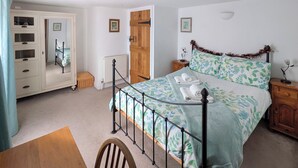 Une chambre à coucher avec un lit, une table de chevet en bois, une commode, un radiateur et une chaise.