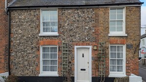 Une maison en pierre à deux étages, avec une porte blanche et deux fenêtres au rez-de-chaussée.
