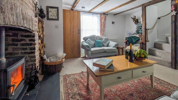 Un salon chaleureux avec une cheminée, un canapé gris, une table basse avec des livres et une plante, et un escalier décor é d’un sapin de Noël.