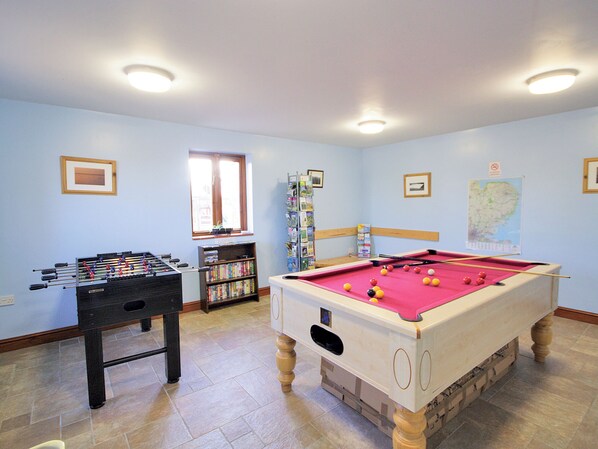 A room with a foosball table, a pool table, and a bookshelf.