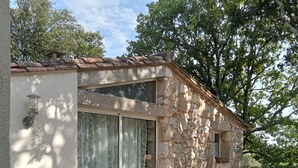 Un edificio in pietra con tetto in tegole, ampie vetrate e un piccolo patio con tavolo e sedie.