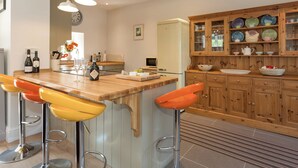 Una cocina con una isla de madera, taburetes de bar, un refrigerador y un armario con vajilla.