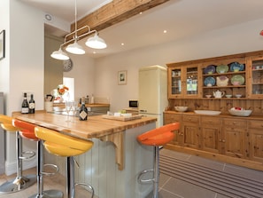 A kitchen with a wooden island, bar stools, a refrigerator, and a cabinet with dishes.