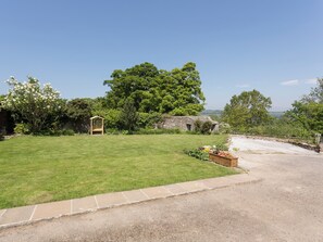 A grassy yard with a stone wall, a wooden structure, and a large tree.