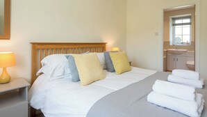 A neatly made bed with pillows, a bedside lamp, and a stack of white towels.