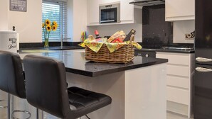 Una cucina moderna con mobili bianchi, un piano di lavoro nero e un cesto di vimini con generi alimentari.