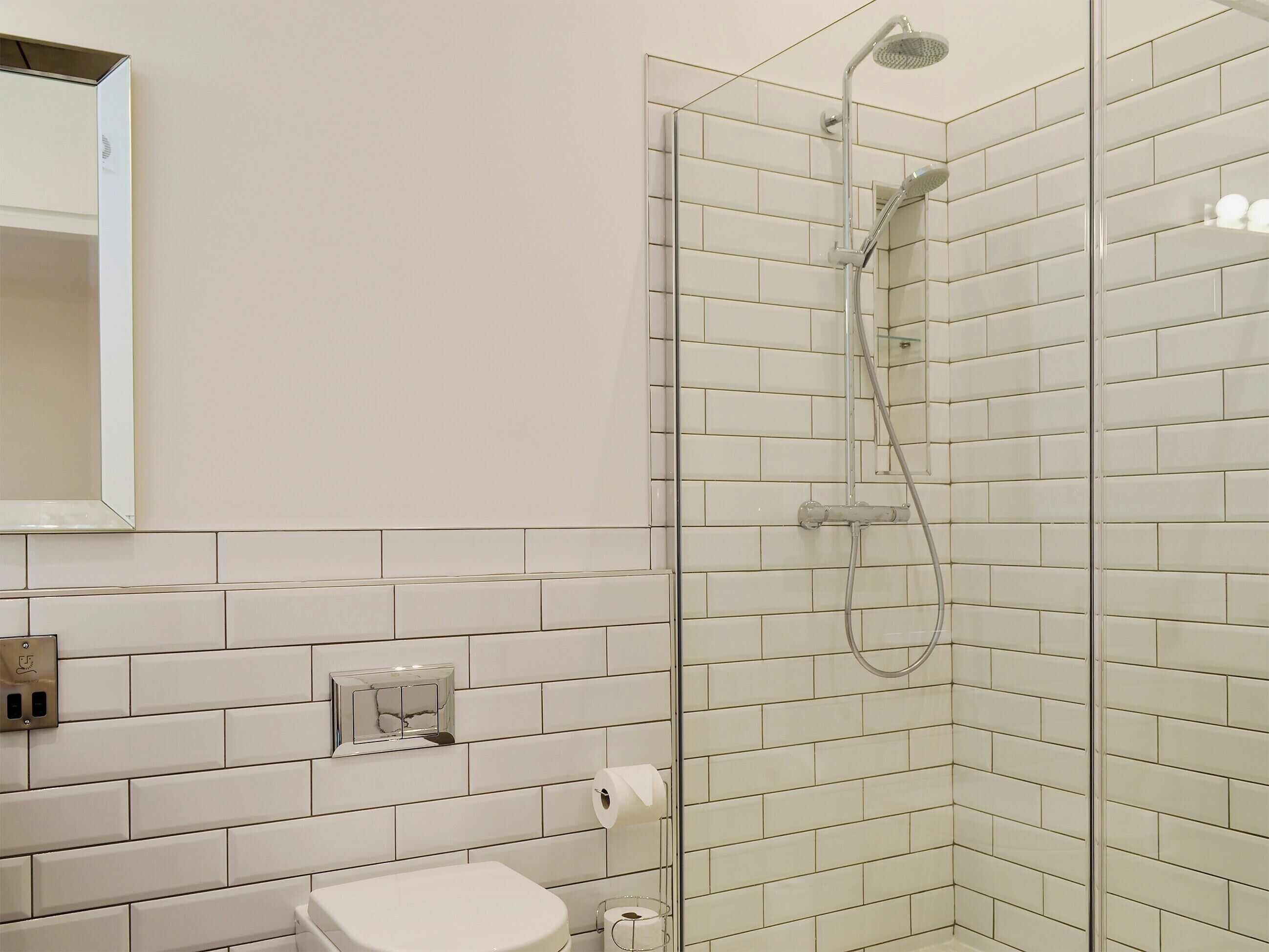 A modern bathroom with a glass-enclosed shower, white tiled walls, a toilet, and a mirror.