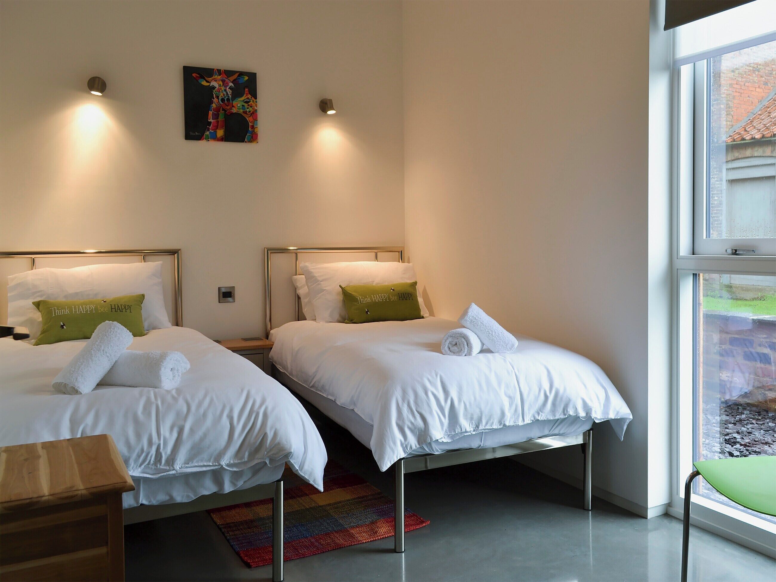 Quarto de hotel com duas camas, um tapete colorido e uma janela com vista para um prédio de tijolos.