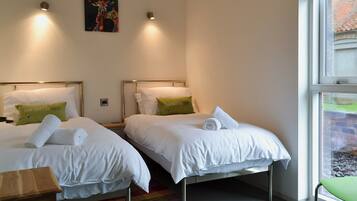 Quarto de hotel com duas camas, um tapete colorido e uma janela com vista para um prédio de tijolos.