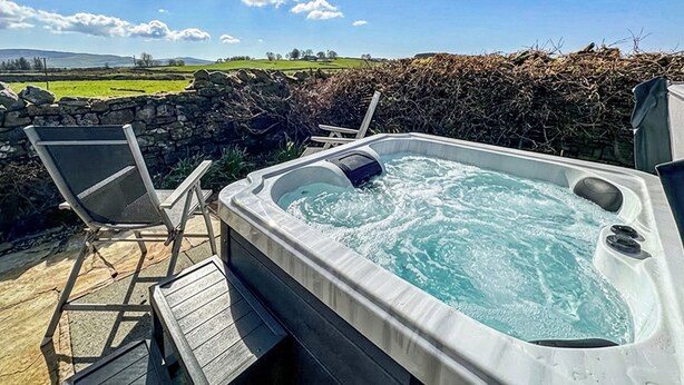 A hot tub with a wooden deck, two chairs, and a stone wall in the background. - 1 bedroom accommodation in North Stainmore, Kirkby Stephen (North Stainmore, Kirkby Stephen)