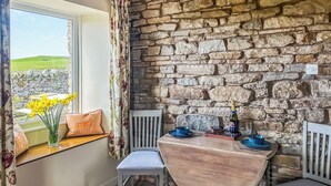 A dining area with a stone wall, a window with daffodils, and a table set for two. - 1 bedroom accommodation in North Stainmore, Kirkby Stephen (North Stainmore, Kirkby Stephen)