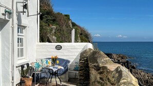 A stone patio with a table and chairs, a potted plant, and a view of the sea. - Puffin Burrow, a beautiful historic couples retreat overlooking the Cove. (Portmellon, near Mevagissey)