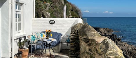 A stone patio with a table and chairs, a potted plant, and a view of the sea.