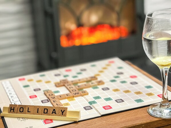 A Scrabble board with the word "HOLIDAY" spelled out, a glass of water, and a fireplace in the background.