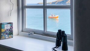 A window with a view of a coastal landscape and a boat. - Puffin Burrow, a beautiful historic couples retreat overlooking the Cove. (Portmellon, near Mevagissey)