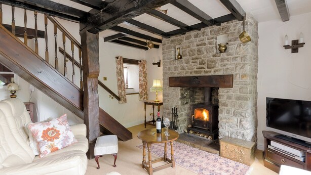 A cozy living room with a stone fireplace, wooden beams, a staircase, and a television. - 3 bedroom accommodation in Bradwell (Bradwell)